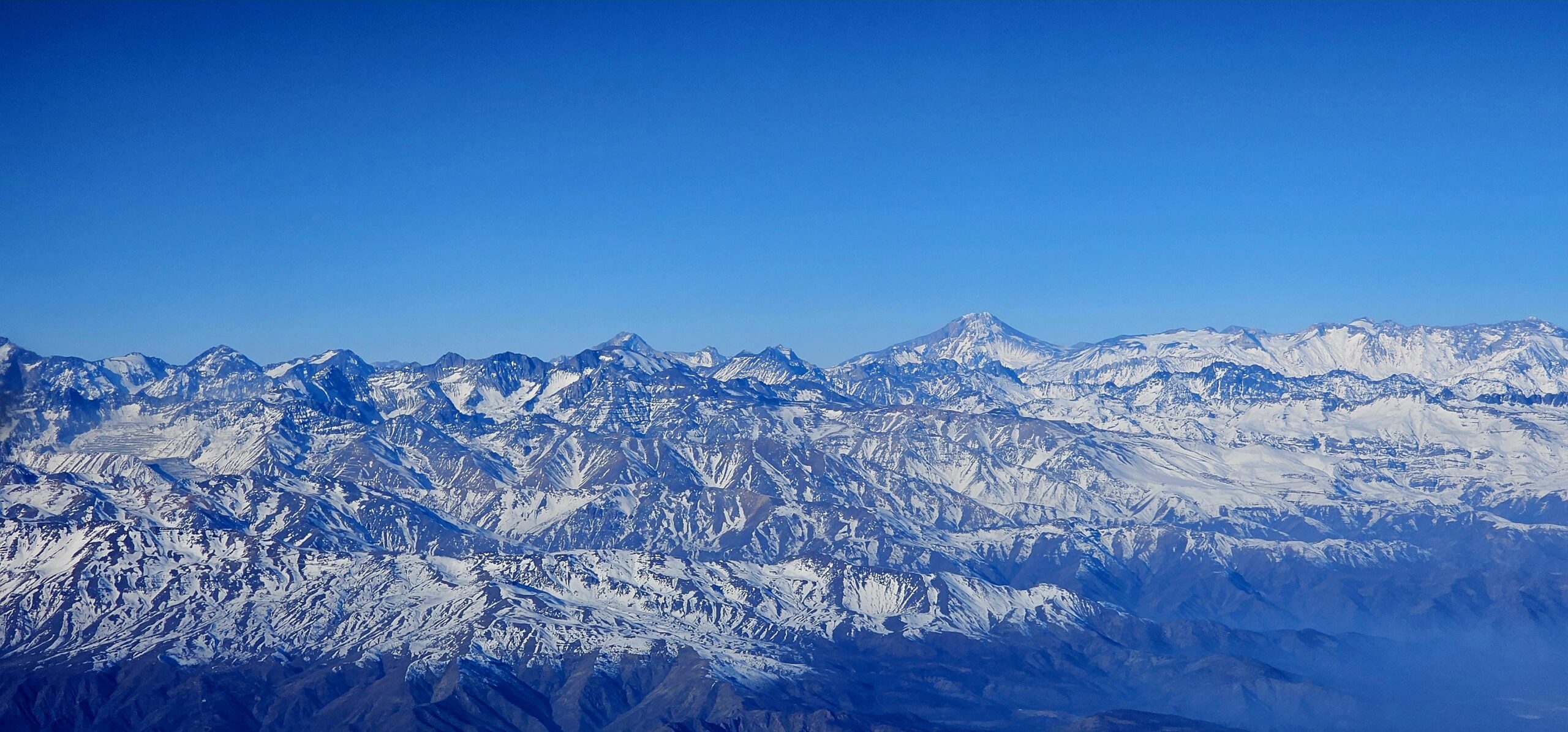 Contact Expansive snow-covered mountain range beneath a clear blue sky